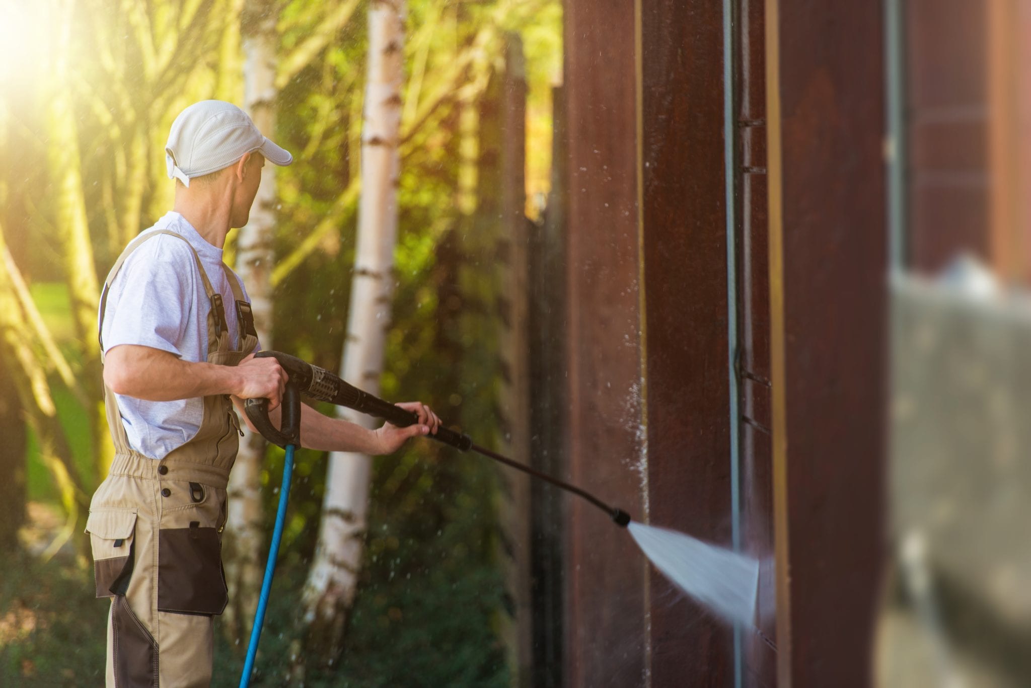 Garage Gate Water Cleaning. Garage Walls and Gate Powerful high Pressure Water Washing. Caucasian Worker Cleaning Building Elements.