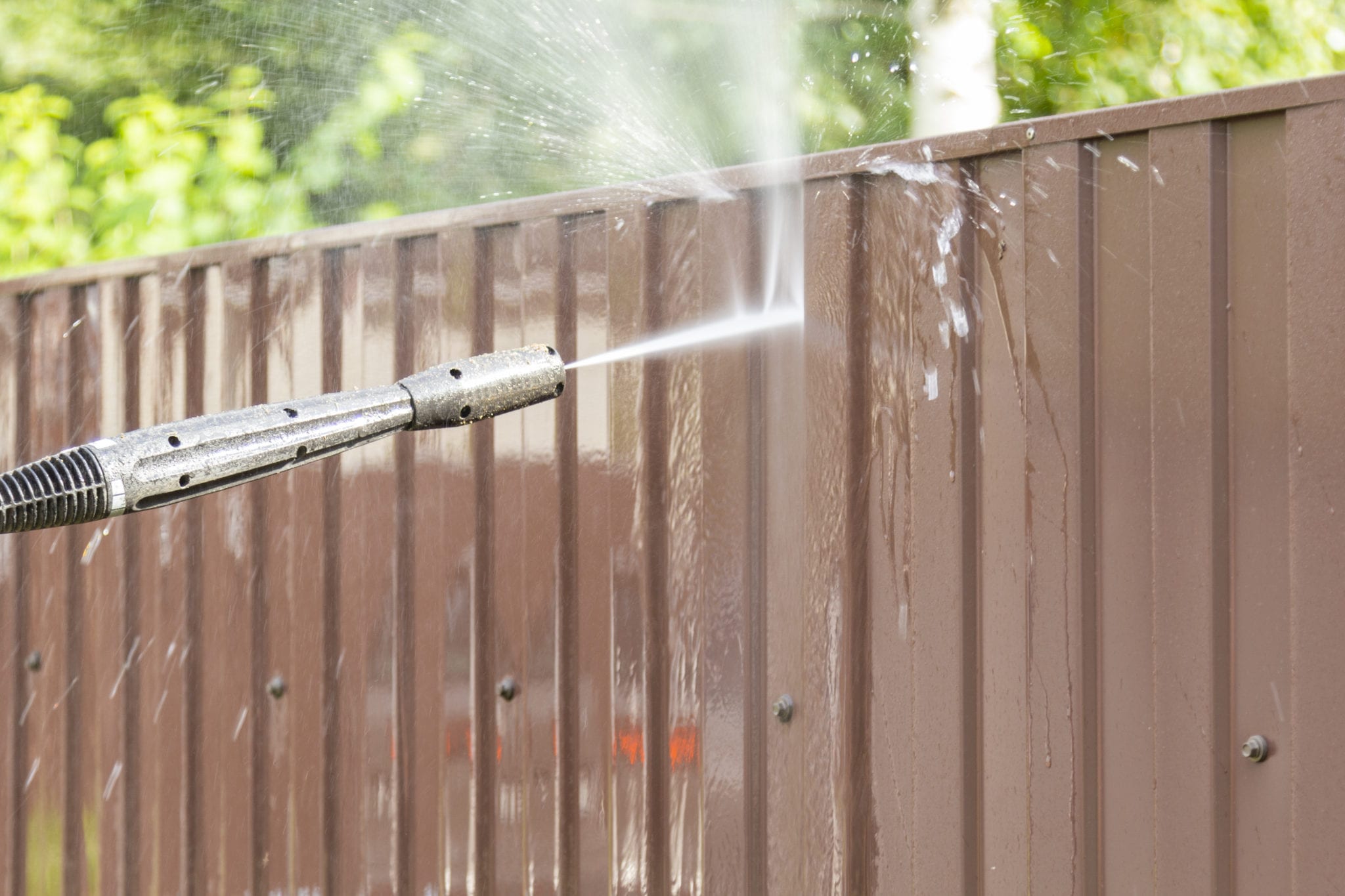 Cleaning fence with high pressure power washer, cleaning dirty wall.