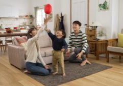cheerful asian dad, mom and son having fun playing hit the ball game in the living room at home. they try to keep the balloon in air